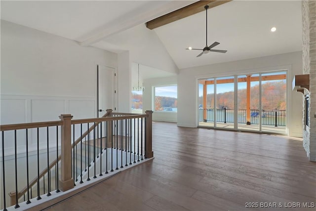 empty room featuring a wainscoted wall, dark wood-style flooring, beamed ceiling, and a decorative wall