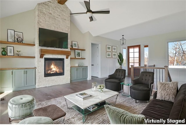 living area with a wainscoted wall, a decorative wall, a large fireplace, ceiling fan, and wood finished floors