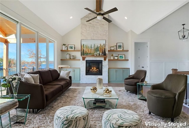 living area with a large fireplace, a ceiling fan, a wainscoted wall, light wood-style flooring, and high vaulted ceiling