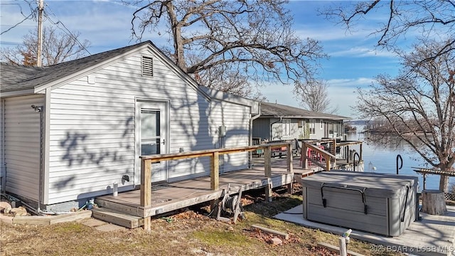 rear view of property featuring a deck with water view and a hot tub