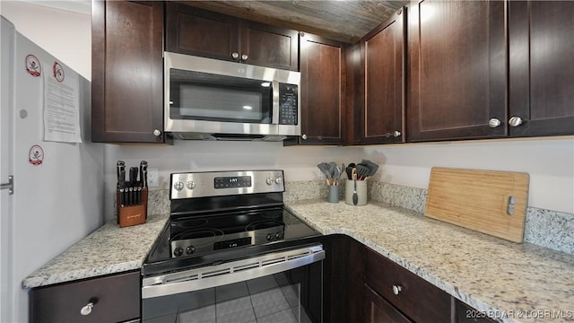 kitchen featuring stainless steel appliances, tile patterned floors, dark brown cabinetry, and light stone counters