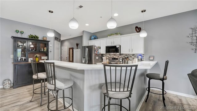 kitchen with stainless steel appliances, white cabinets, a kitchen breakfast bar, and decorative light fixtures