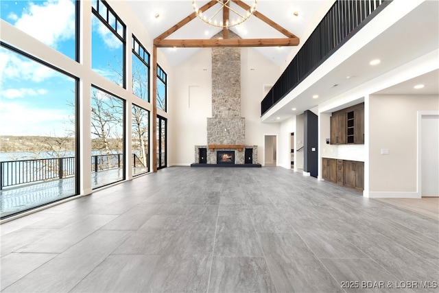 unfurnished living room featuring an inviting chandelier, a stone fireplace, high vaulted ceiling, and beamed ceiling