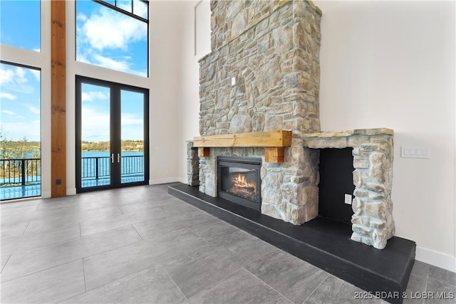 unfurnished living room featuring a water view, a towering ceiling, a fireplace, and french doors