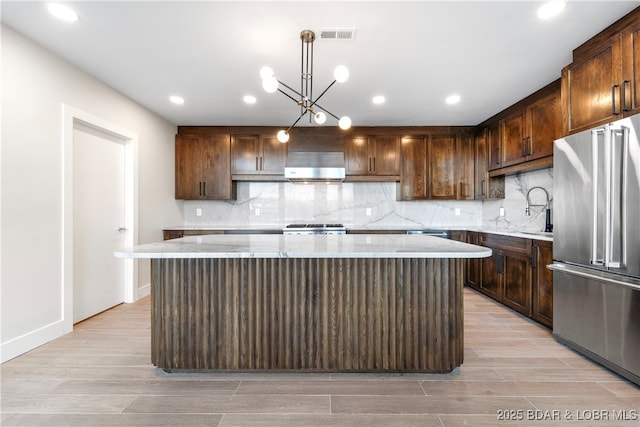 kitchen with pendant lighting, a center island, high end refrigerator, and light wood-type flooring