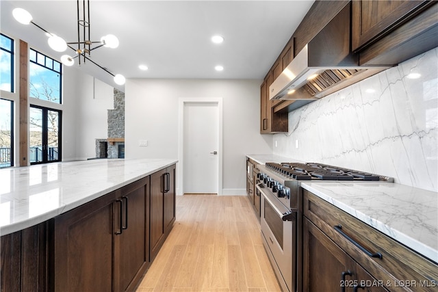 kitchen with stainless steel stove, decorative light fixtures, tasteful backsplash, custom exhaust hood, and light stone countertops