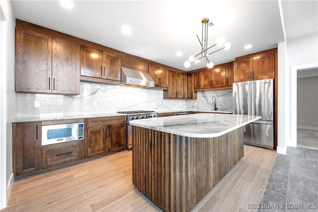 kitchen featuring wall chimney range hood, sink, hanging light fixtures, high end appliances, and a kitchen island