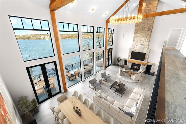 living room featuring a water view, a stone fireplace, high vaulted ceiling, and a wealth of natural light