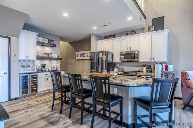 kitchen featuring white cabinetry, beverage cooler, a kitchen bar, stainless steel appliances, and light hardwood / wood-style flooring