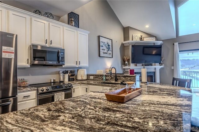 kitchen featuring vaulted ceiling, white cabinetry, sink, dark stone countertops, and stainless steel appliances