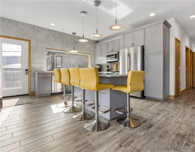 kitchen with gray cabinets, appliances with stainless steel finishes, hanging light fixtures, and light hardwood / wood-style flooring