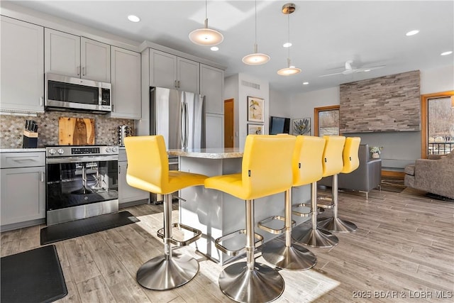 kitchen with gray cabinets, pendant lighting, a kitchen bar, light hardwood / wood-style floors, and stainless steel appliances