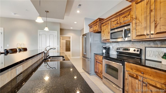 kitchen with sink, dark stone countertops, stainless steel appliances, tasteful backsplash, and decorative light fixtures