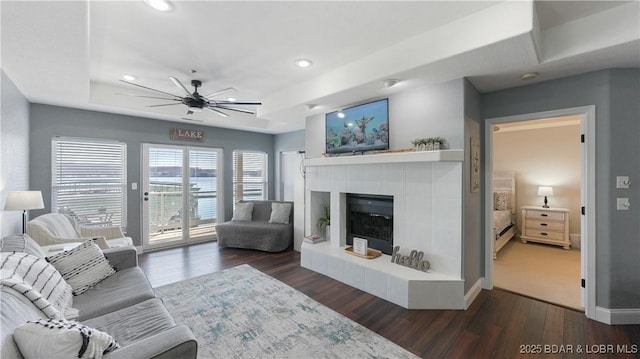 living room featuring dark hardwood / wood-style floors, ceiling fan, a tray ceiling, and a tile fireplace