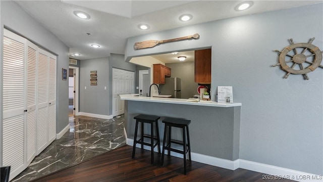 kitchen featuring sink, stainless steel fridge, a kitchen breakfast bar, dark hardwood / wood-style floors, and kitchen peninsula