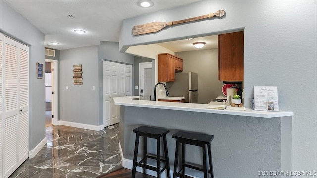 kitchen with stainless steel refrigerator, a kitchen bar, kitchen peninsula, and sink