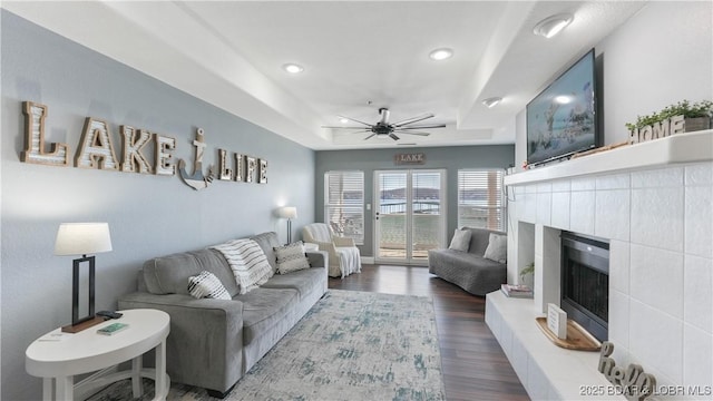 living room with ceiling fan, a fireplace, a tray ceiling, and dark hardwood / wood-style flooring