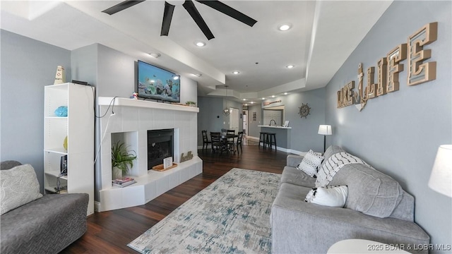 living room with ceiling fan, a fireplace, dark hardwood / wood-style floors, and a raised ceiling