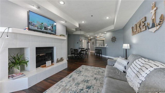 living room with dark hardwood / wood-style flooring, a tiled fireplace, and a raised ceiling