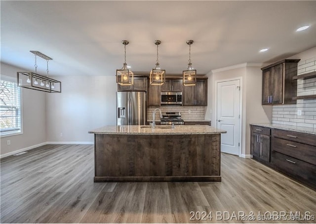 kitchen featuring dark brown cabinetry, light stone counters, stainless steel appliances, and a center island with sink