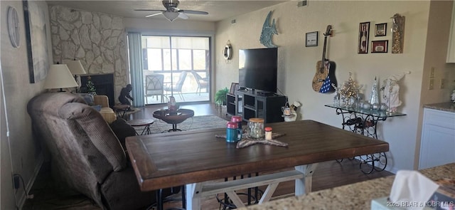 dining space with a stone fireplace and ceiling fan