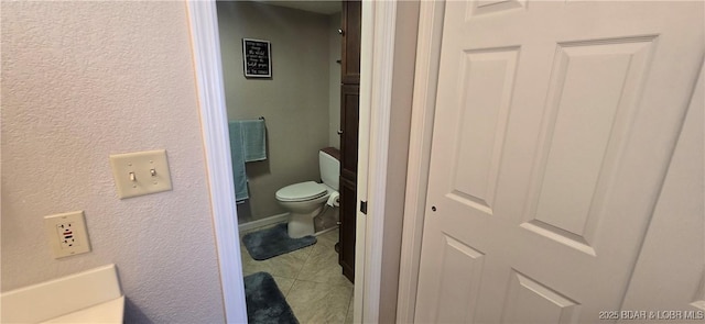 bathroom with tile patterned floors, toilet, and a textured wall