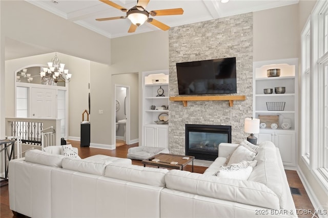 living room with dark wood-type flooring, ornamental molding, a stone fireplace, and built in features