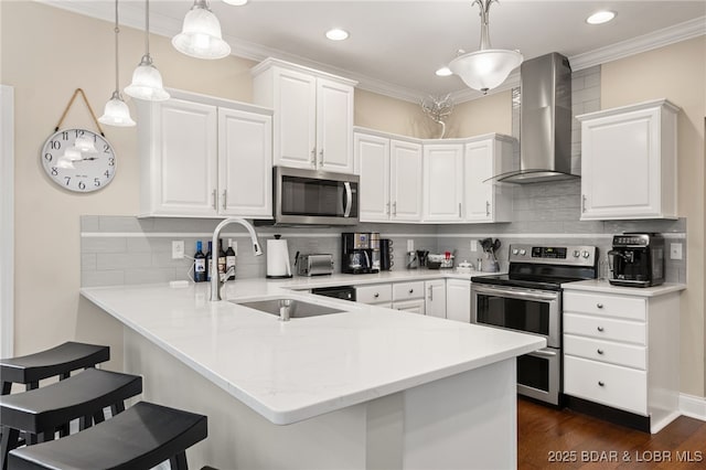 kitchen with pendant lighting, white cabinets, wall chimney exhaust hood, and appliances with stainless steel finishes