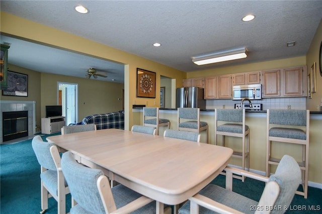 dining area with a tiled fireplace, a textured ceiling, carpet floors, and ceiling fan