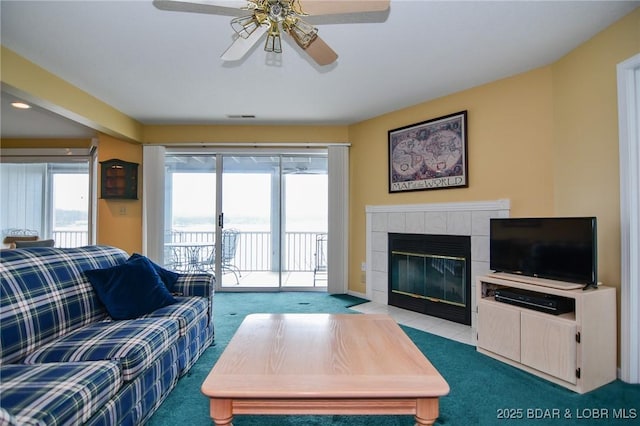 living room with a tile fireplace, light colored carpet, and ceiling fan