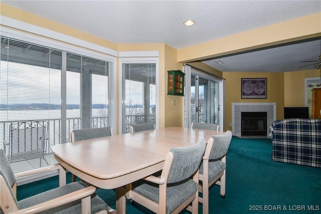 dining space featuring a water view, carpet floors, a textured ceiling, and a fireplace