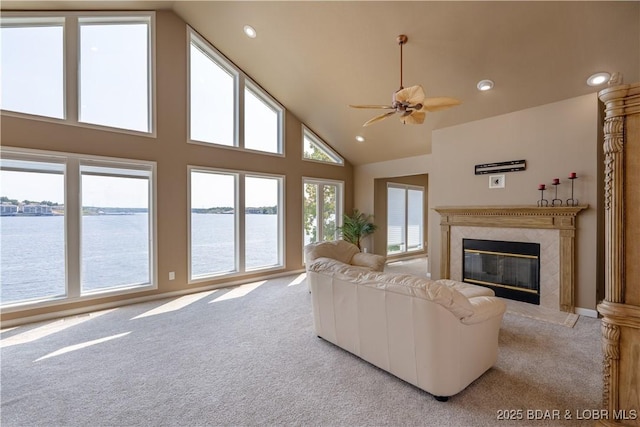 living room featuring light carpet, high vaulted ceiling, a premium fireplace, and a water view