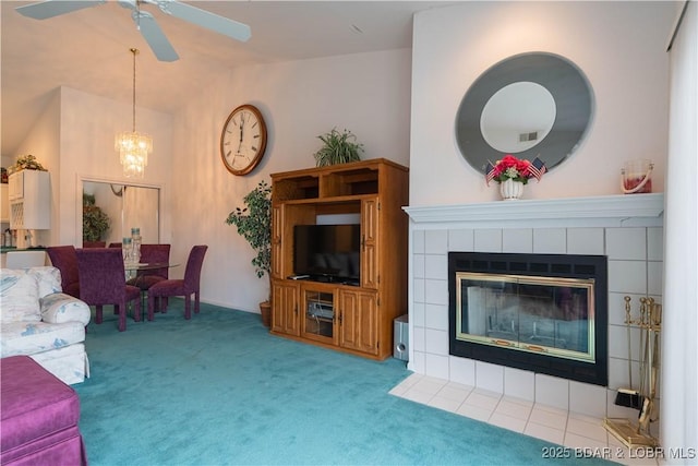 carpeted living room featuring ceiling fan with notable chandelier, vaulted ceiling, and a tile fireplace