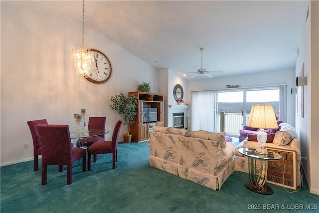 carpeted living room featuring a tiled fireplace, vaulted ceiling, and ceiling fan with notable chandelier