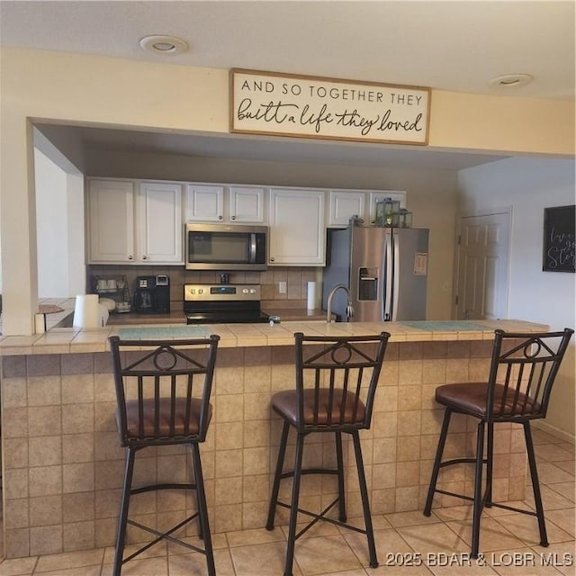 kitchen featuring a breakfast bar area, appliances with stainless steel finishes, kitchen peninsula, decorative backsplash, and white cabinets