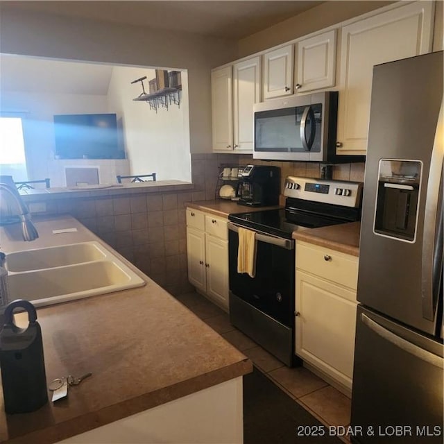 kitchen featuring white cabinetry, appliances with stainless steel finishes, dark tile patterned flooring, and sink