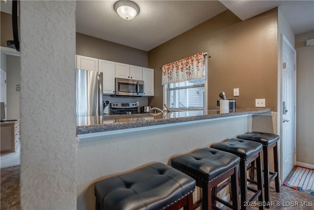 kitchen with appliances with stainless steel finishes, a kitchen breakfast bar, kitchen peninsula, tile patterned flooring, and white cabinets