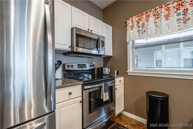 kitchen with stainless steel appliances, dark stone counters, and white cabinets