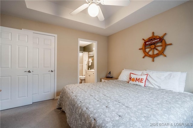 carpeted bedroom featuring ensuite bath, a raised ceiling, and ceiling fan