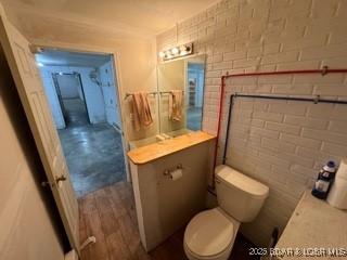 bathroom featuring brick wall, vanity, toilet, and hardwood / wood-style floors