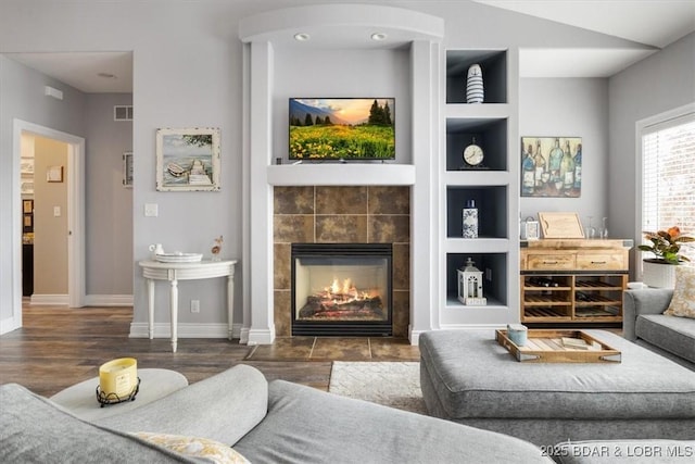 living room featuring a tiled fireplace, dark hardwood / wood-style flooring, and built in shelves