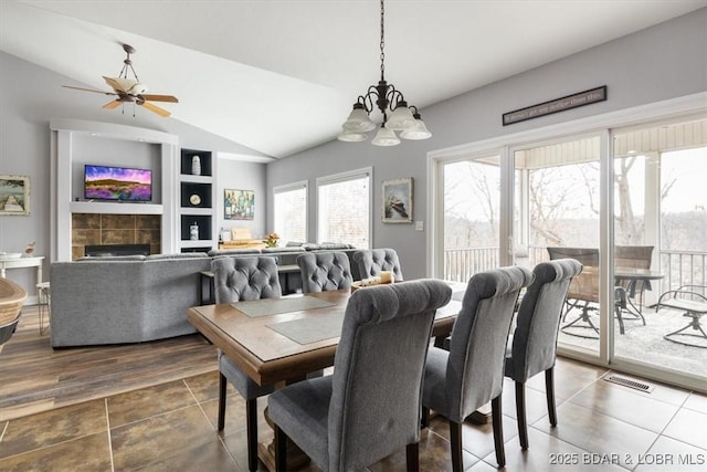 dining area featuring lofted ceiling, built in shelves, a fireplace, and ceiling fan with notable chandelier