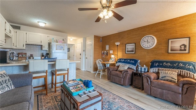 living room with ceiling fan, a textured ceiling, and light hardwood / wood-style floors