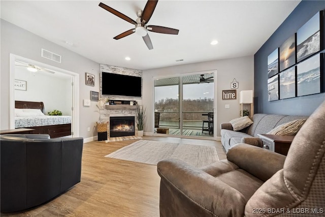 living room featuring a stone fireplace, ceiling fan, and light wood-type flooring