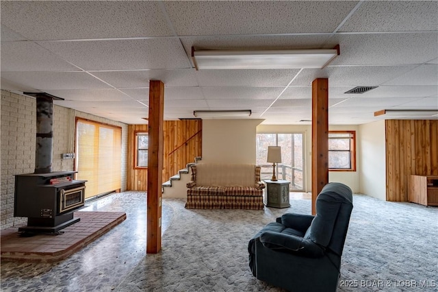 basement with carpet, a wood stove, and a drop ceiling