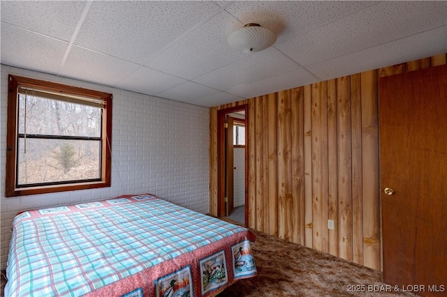 carpeted bedroom featuring a paneled ceiling, wooden walls, and brick wall