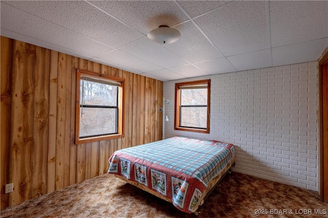 carpeted bedroom with brick wall, a paneled ceiling, and wooden walls