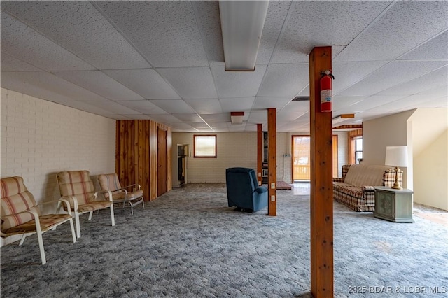 basement featuring brick wall, carpet floors, and a paneled ceiling