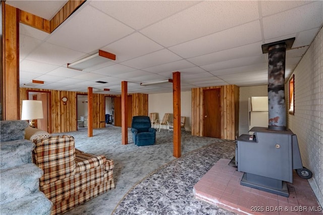 interior space with a paneled ceiling, wooden walls, and a wood stove