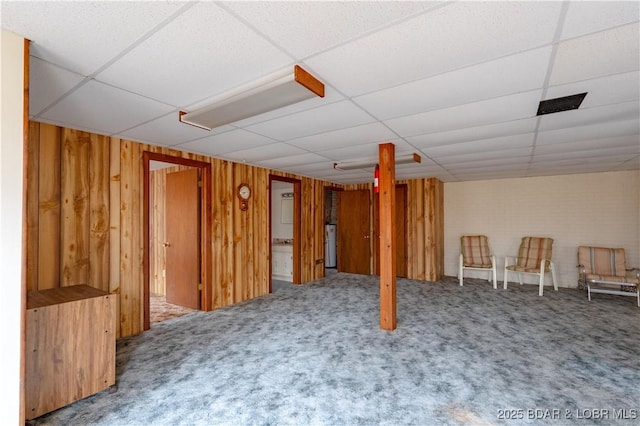 basement featuring a drop ceiling, wooden walls, and carpet